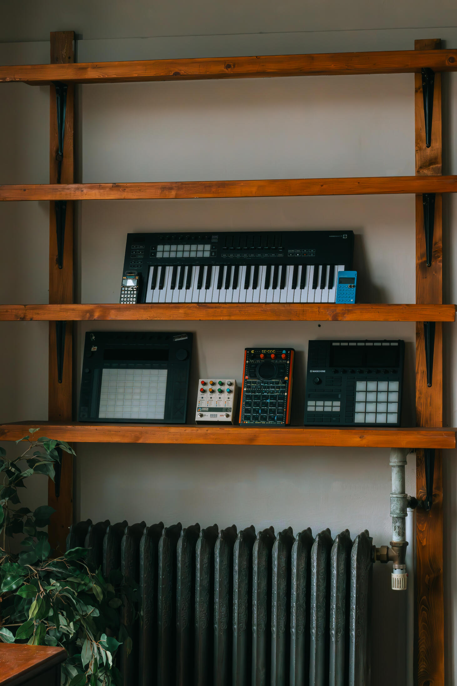 Multiple high-quality MIDI pianos and devices used to produce, mix, and master different music tracks, featured on a clean wood shelf with light shining on them.