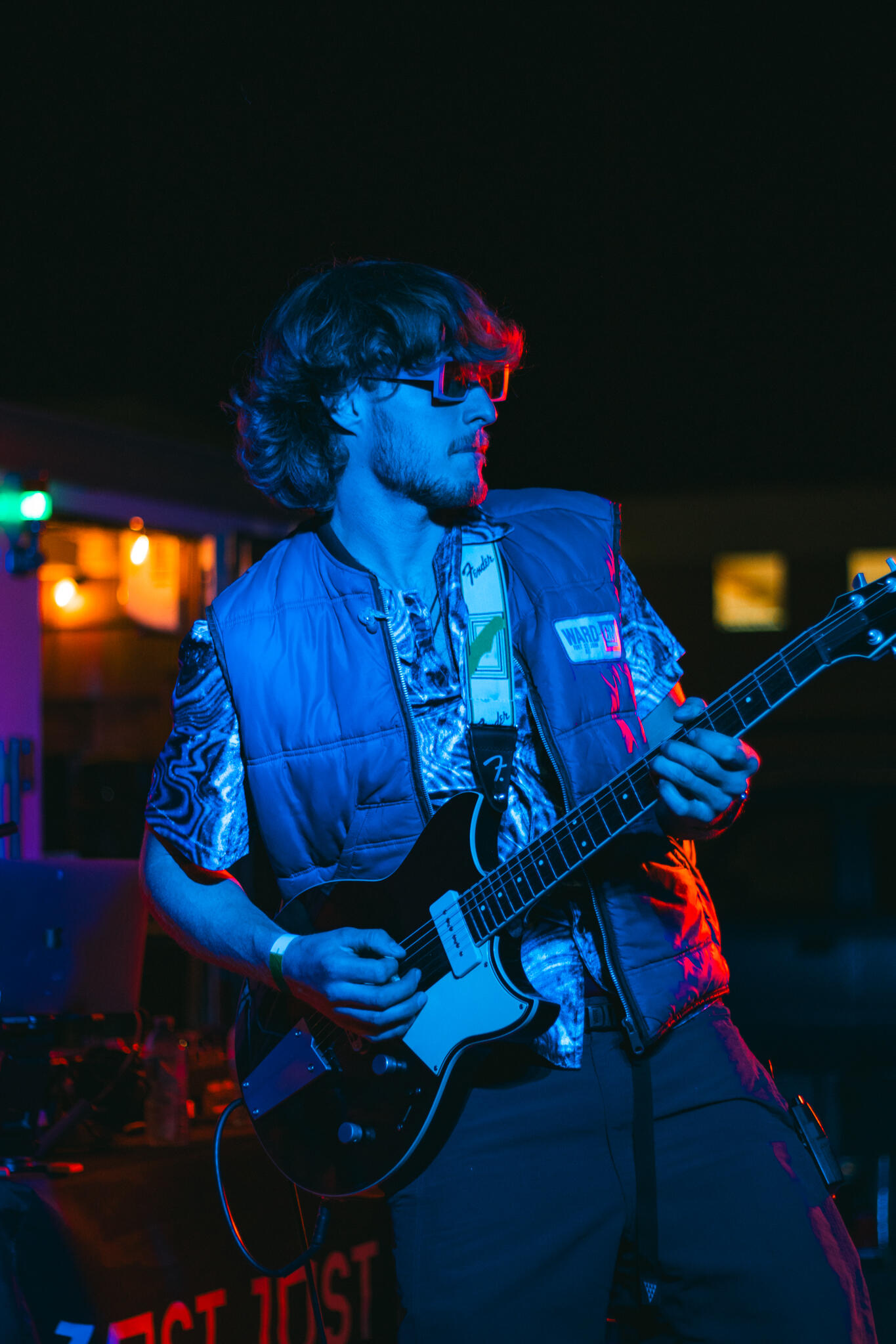 A man playing an electric guitar at Vice and Virtue brewery, immersed in his performance, with a warm neon ambiance surrounding him.