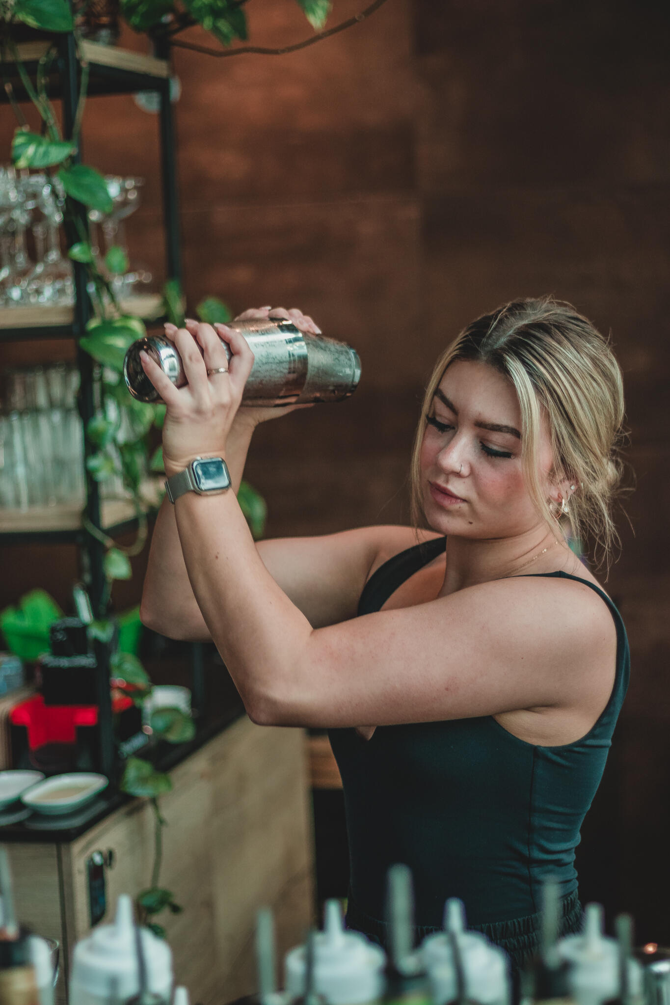 A woman mixes a cocktail at a bar, showcasing her bartending skills amidst an array of colorful liquor bottles.