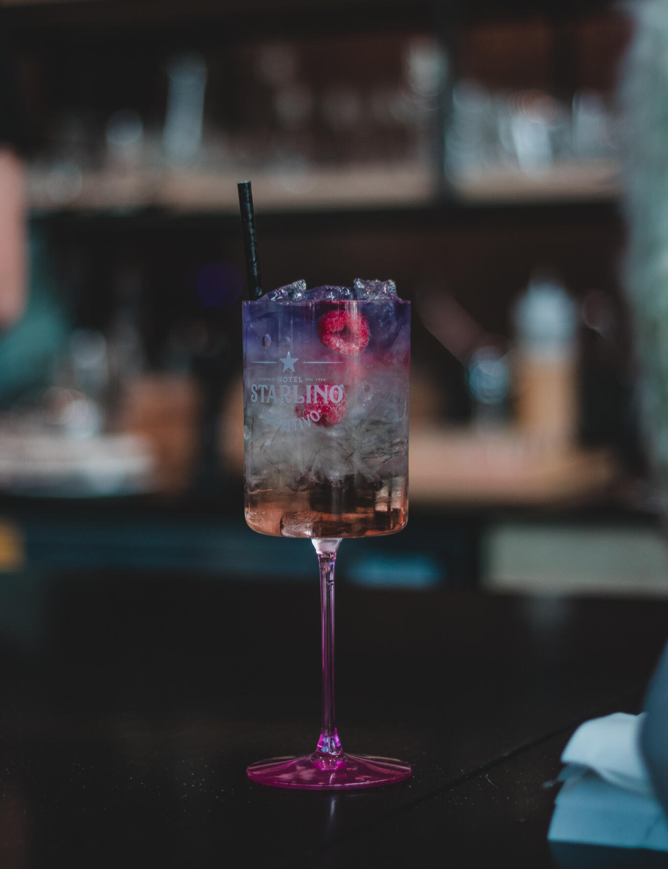 A vibrant purple cocktail drink in a pink glass, elegantly placed on a polished bar surface.