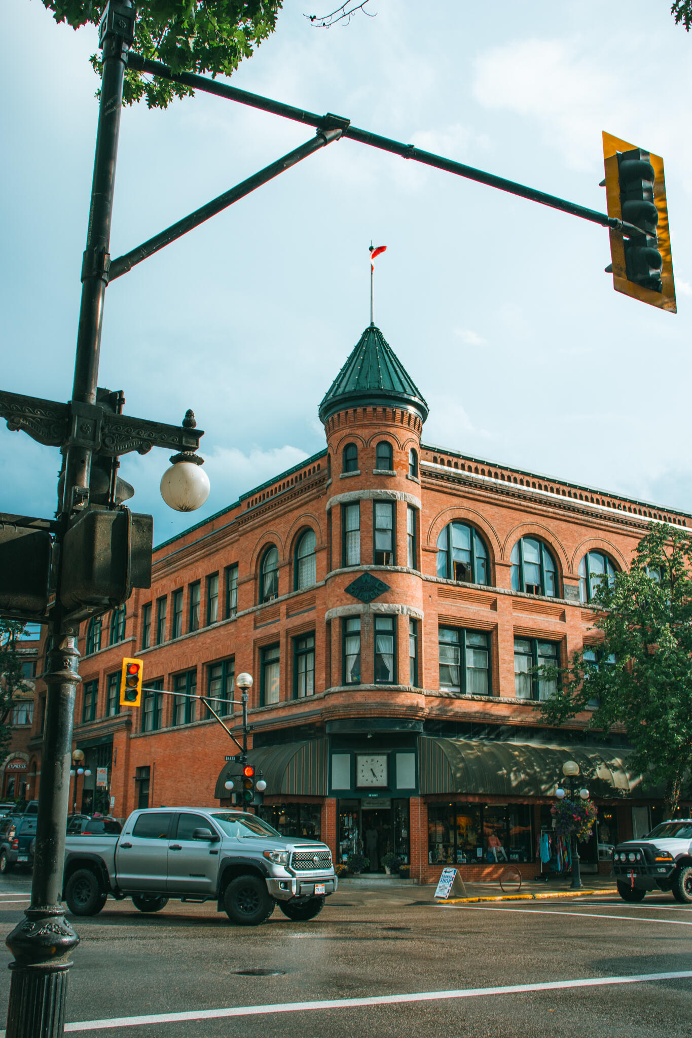 A towering old English Victorian style building with a distinctive clock tower, showcasing architectural details against a bright sky and a busy intersection of cars.