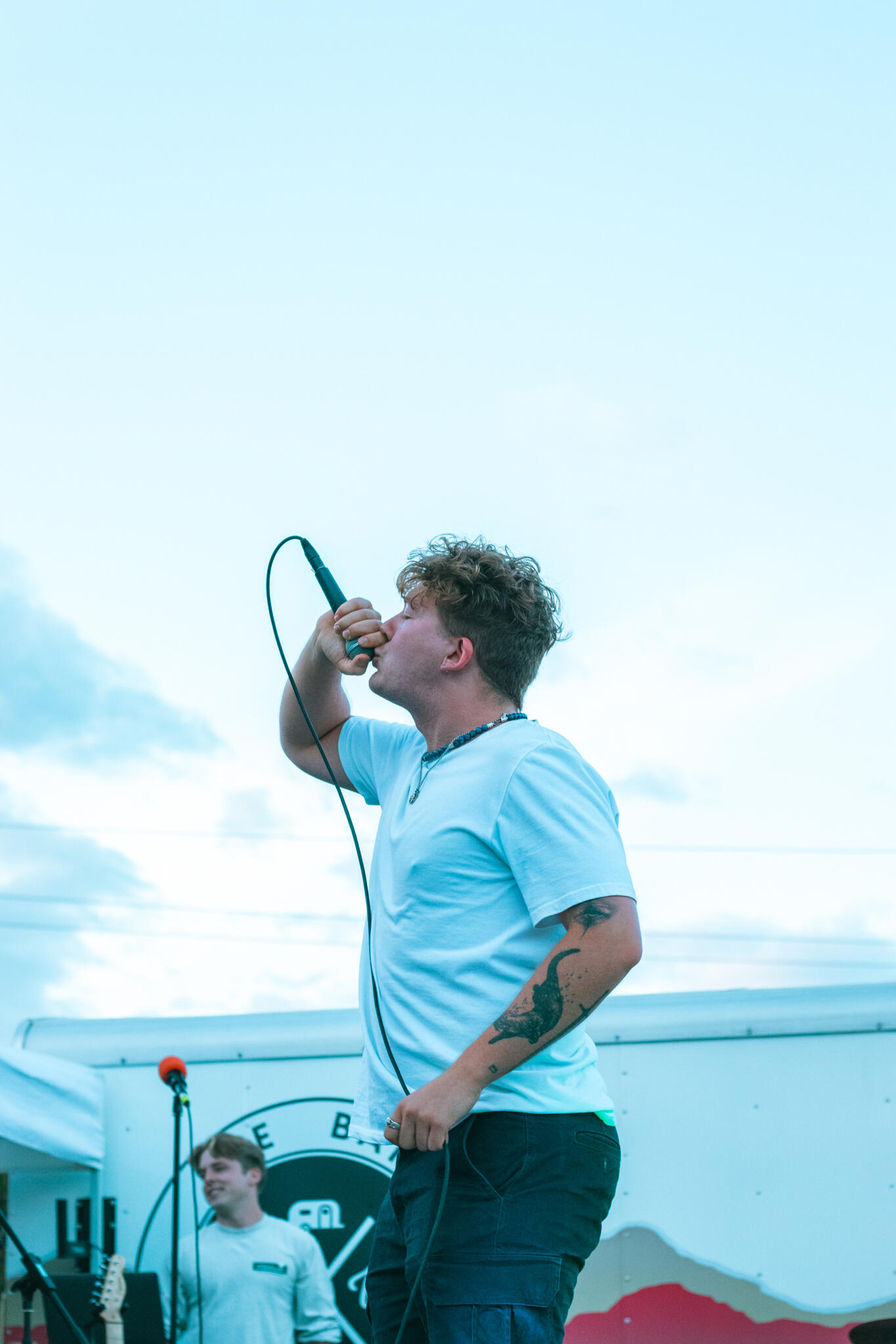 A man with tattoos on his arms sings into a microphone, expressing emotion through his performance.