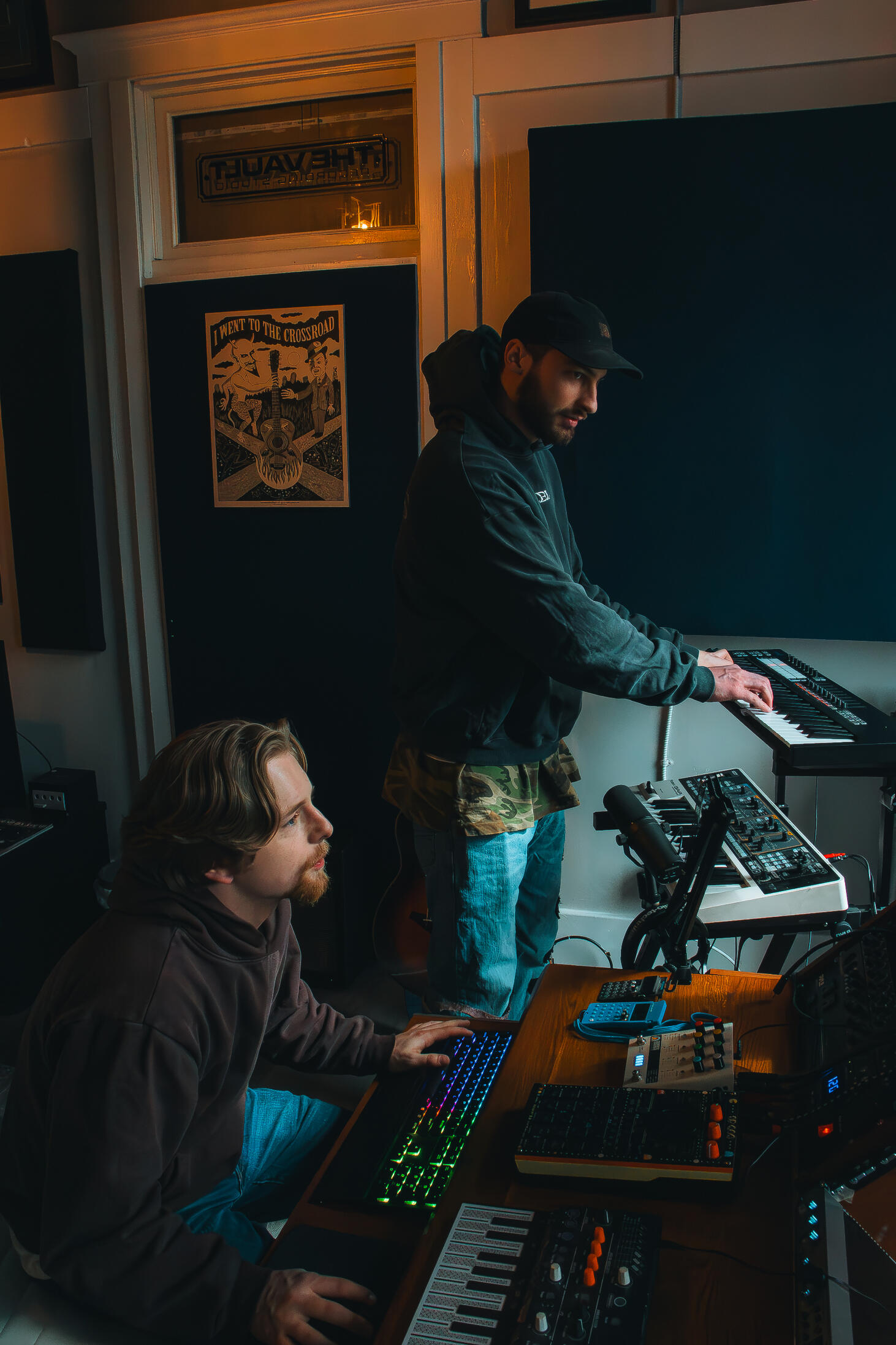 Multiple high-quality MIDI pianos and devices used to produce, mix, and master different music tracks, featured on a clean wood shelf with light shining on them.